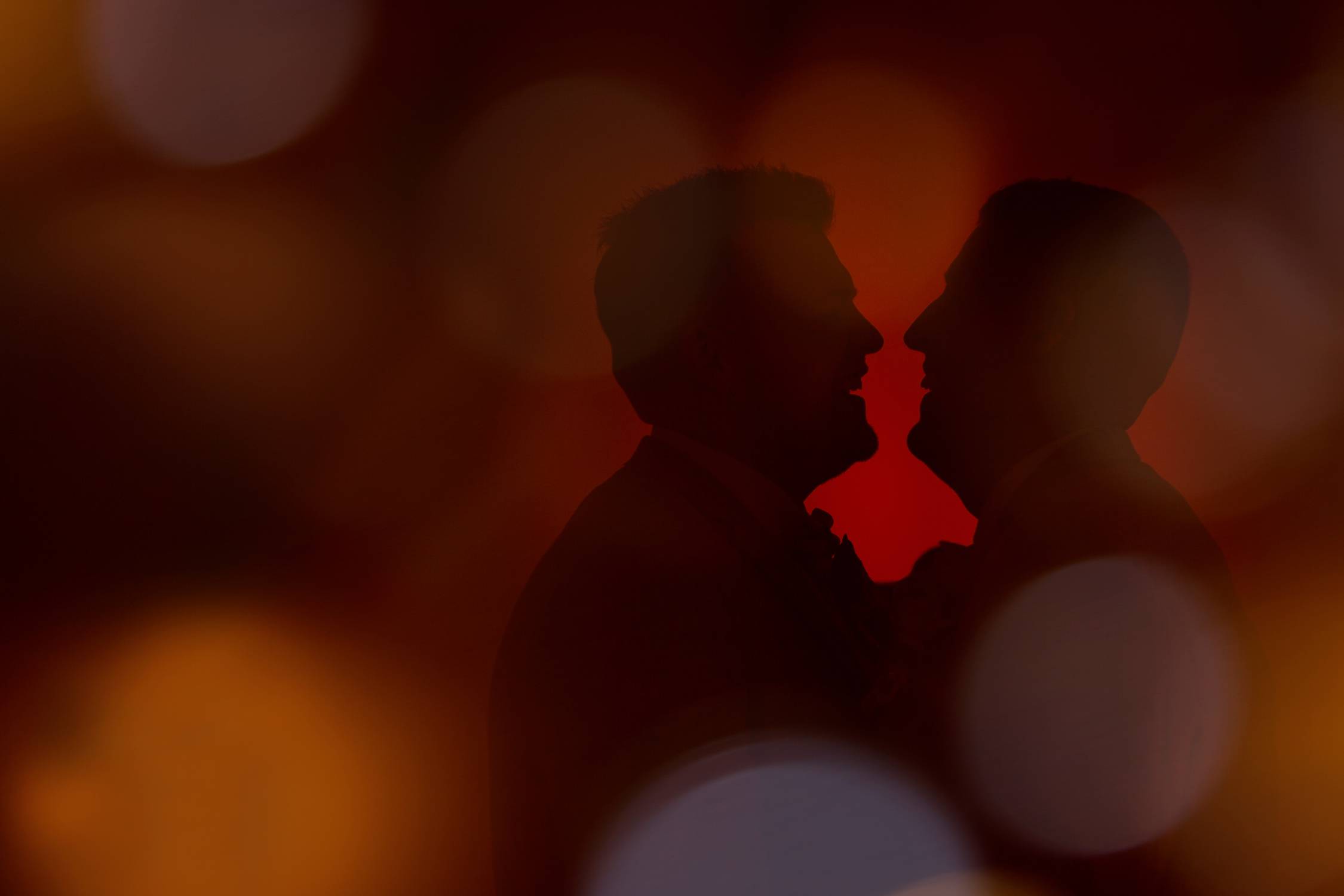 Silhouette of two men kissing in front of a red light, featuring Shaun & Chris.