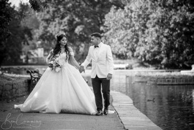 Black and white photo of a bride and groom walking by a pond.