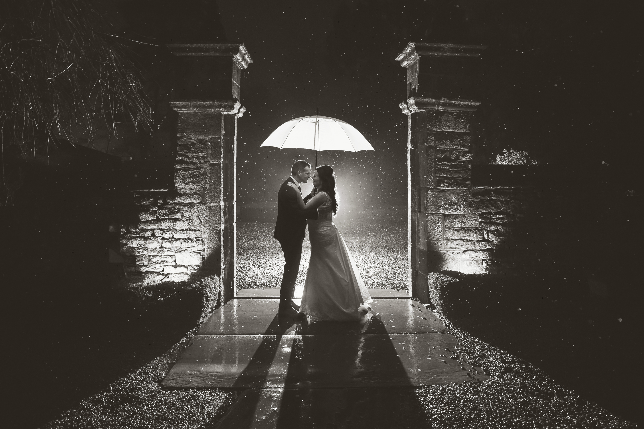A bride and groom standing under an umbrella in the dark.