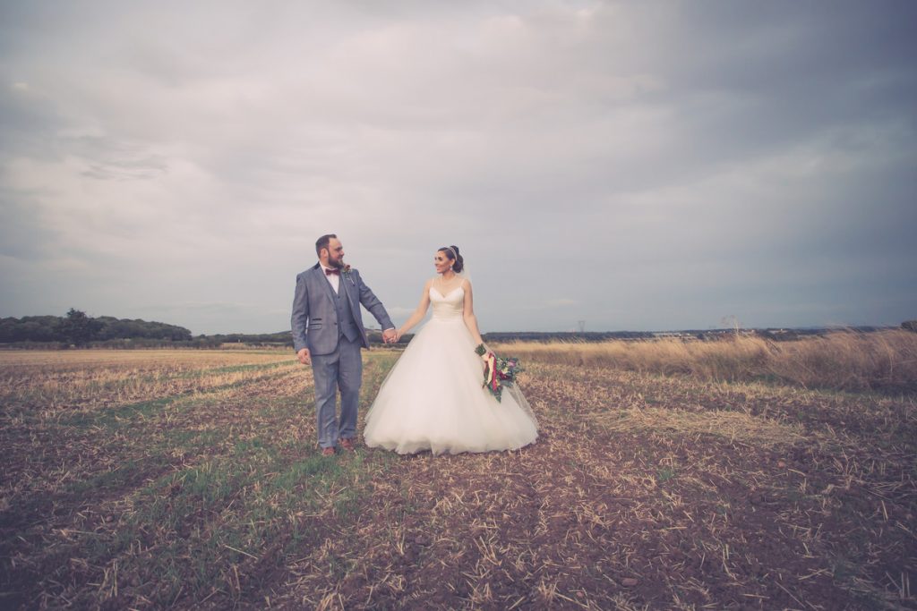A Sheffield wedding photographer capturing a bride and groom standing in a field under a cloudy sky.