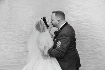 A newlywed couple kisses near a serene body of water, showcasing their wedding portfolio.